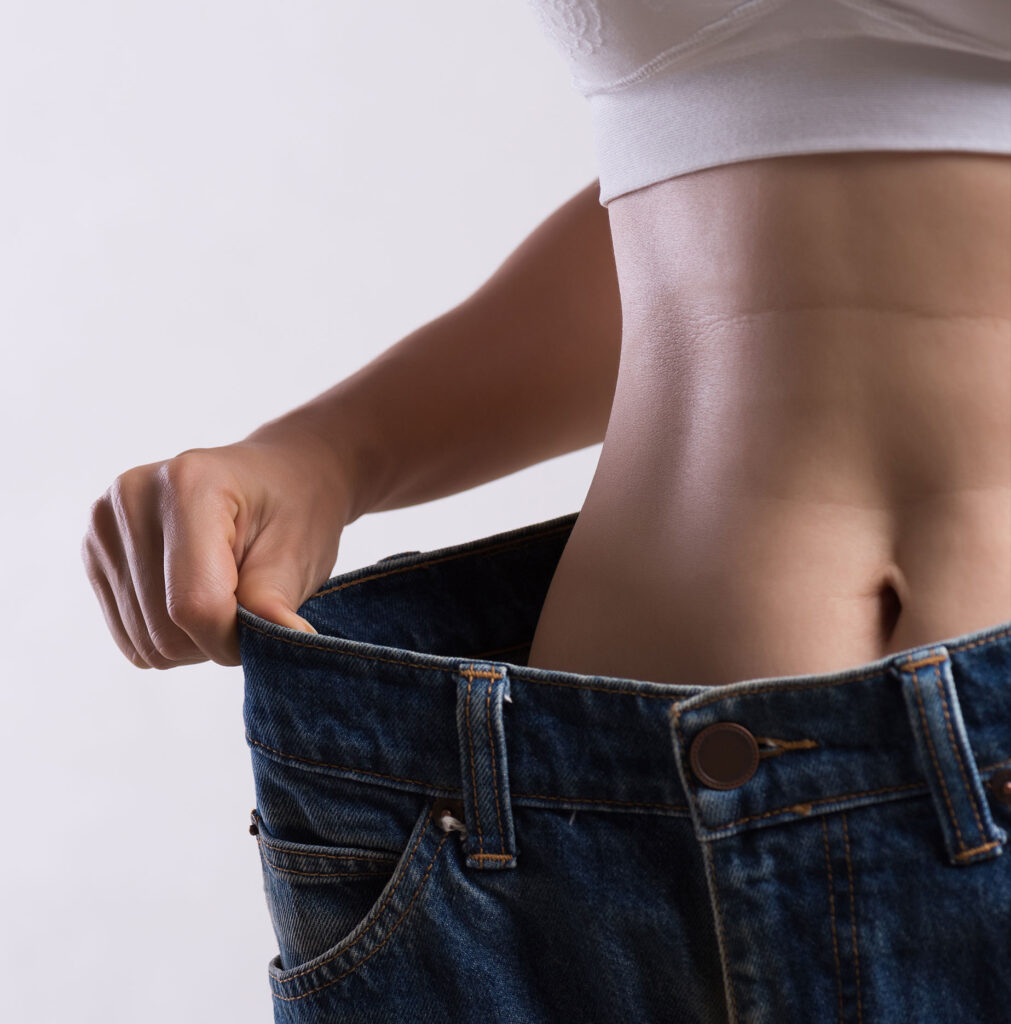 Person zeigt schlanke Taille in zu großen Hosen – Symbolbild für erfolgreiche Ernährungsmedizin und Gewichtsreduktion.